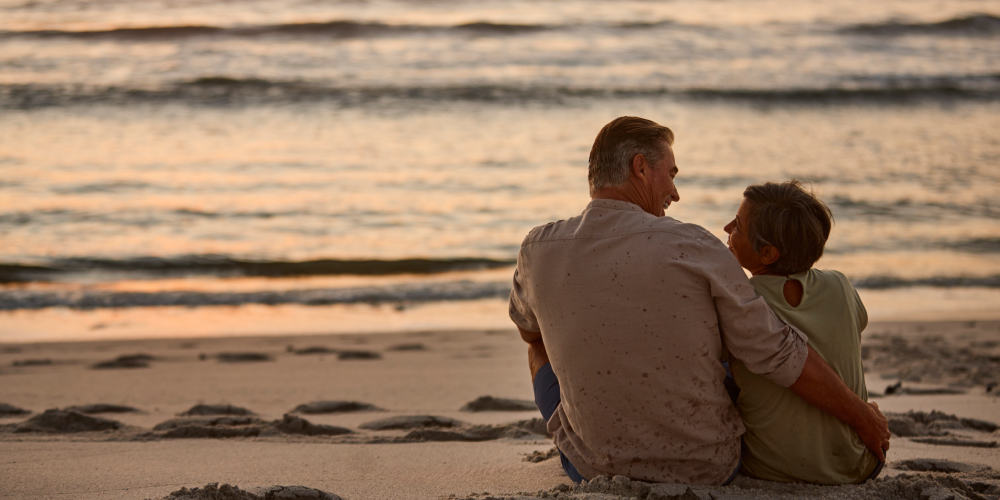 Para siedzi na tle morza, symbolizując relaks i bliskość w związku, z akcentem na poprawę jakości życia seksualnego w okresie menopauzy
