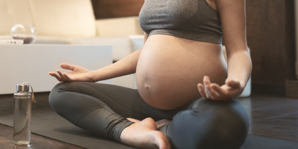 Kobieta w ciąży w pozycji medytacyjnej podczas ćwiczeń relaksacyjnych jogi wspierających zdrowie i dobre samopoczucie