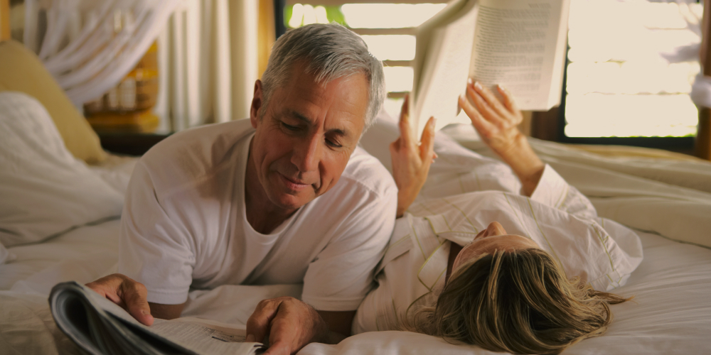 Dojrzały mężczyzna i kobieta leżący na łóżku i czytający książki – andropauza a jakość życia codziennego