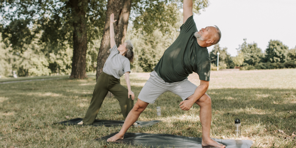 Dojrzała para ćwicząca jogę na świeżym powietrzu w parku – aktywność fizyczna jako sposób na łagodzenie objawów andropauzy